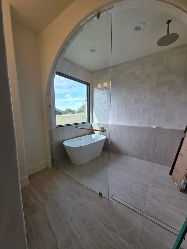 Teton Valley home: Tall fixed frameless glass panel separating a freestanding tub and curbless walk-in shower under an arched opening