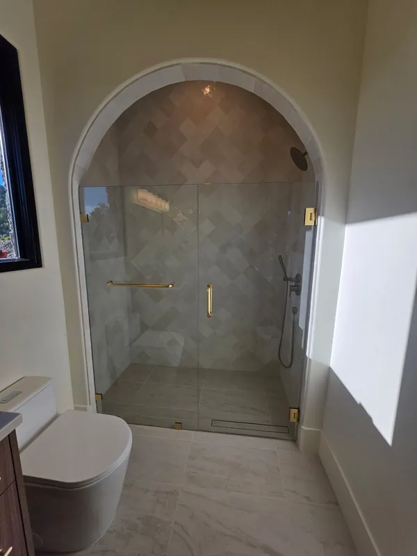 Teton Valley home: Frameless door and panel with brushed gold hardware in an arched shower with diamond-pattern tile