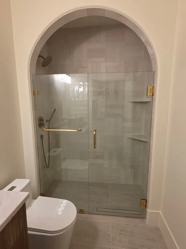 Teton Valley home: Frameless door and panel in an arched shower with towel bar on the glass and brushed gold hardware